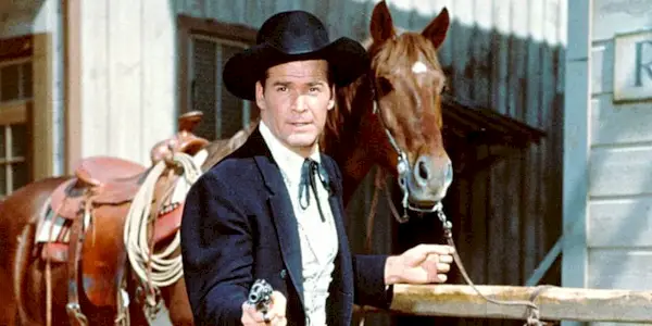 James Garner standing in front of a horse with his gun drawn in Maverick