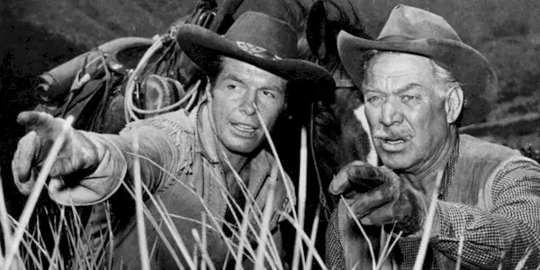 Ward Bond and Robert Horton crouching down in a field in Wagon Train
