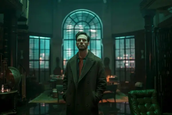 Sam Claflin in Lazarus, stood in a room in front of a window in the dark.